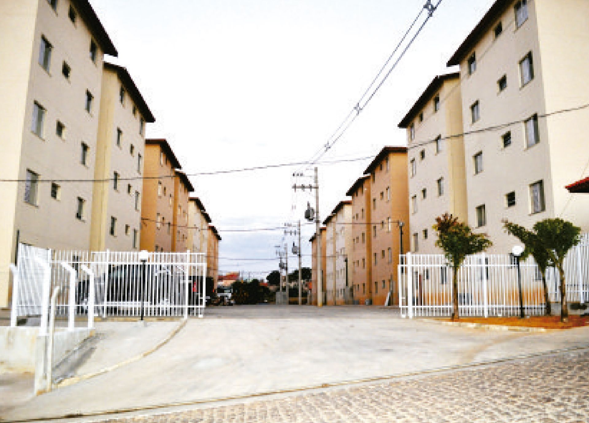Prédios de apartamentos com paredes bege, cercas brancas e entrada pavimentada.