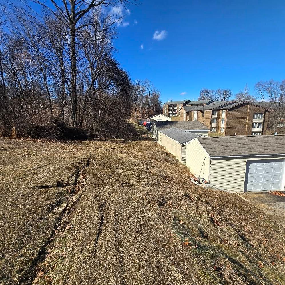 A dirt road leading to a house with a garage and trees in the background.
