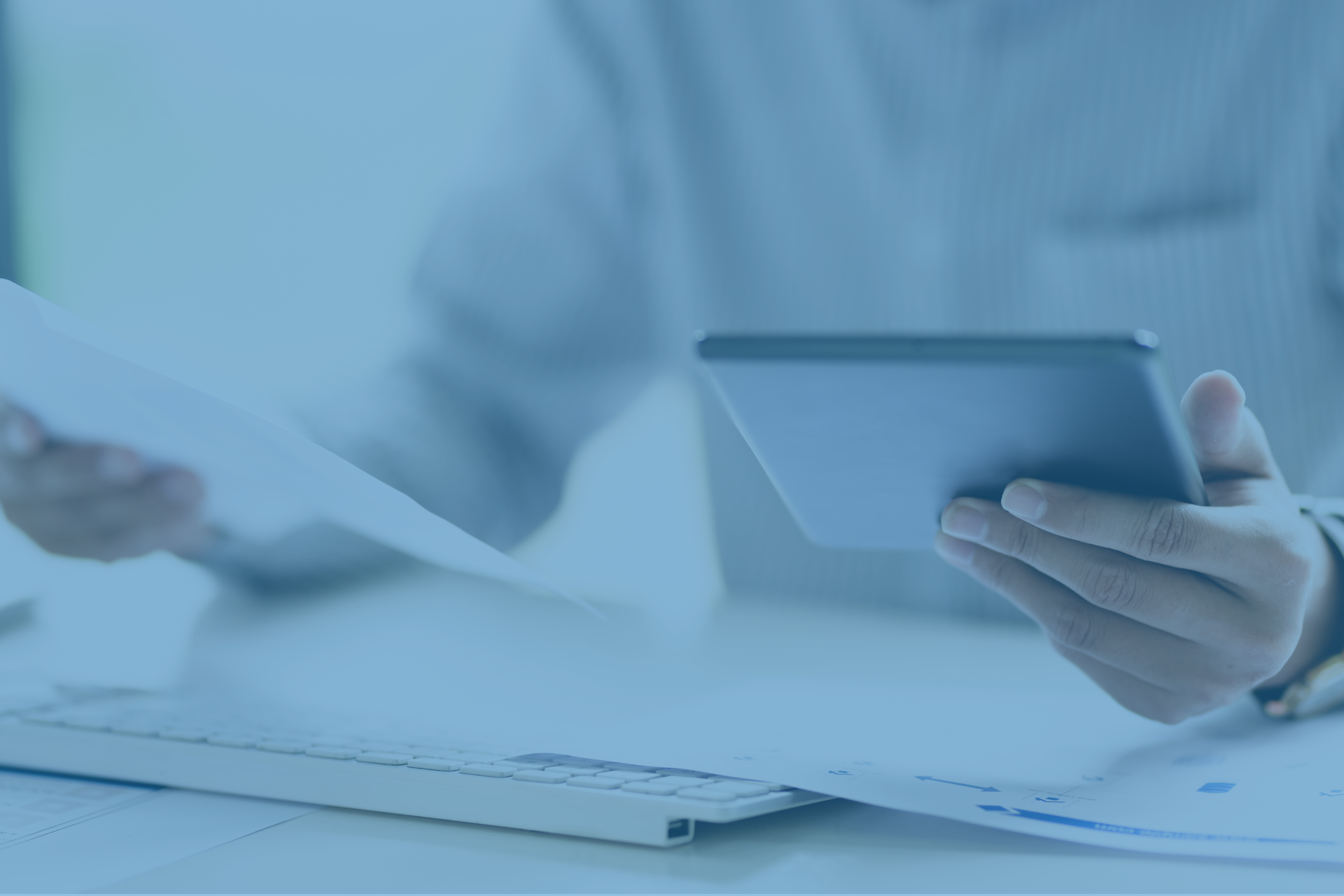 A person at a desk cross-referencing a printed document with a tablet