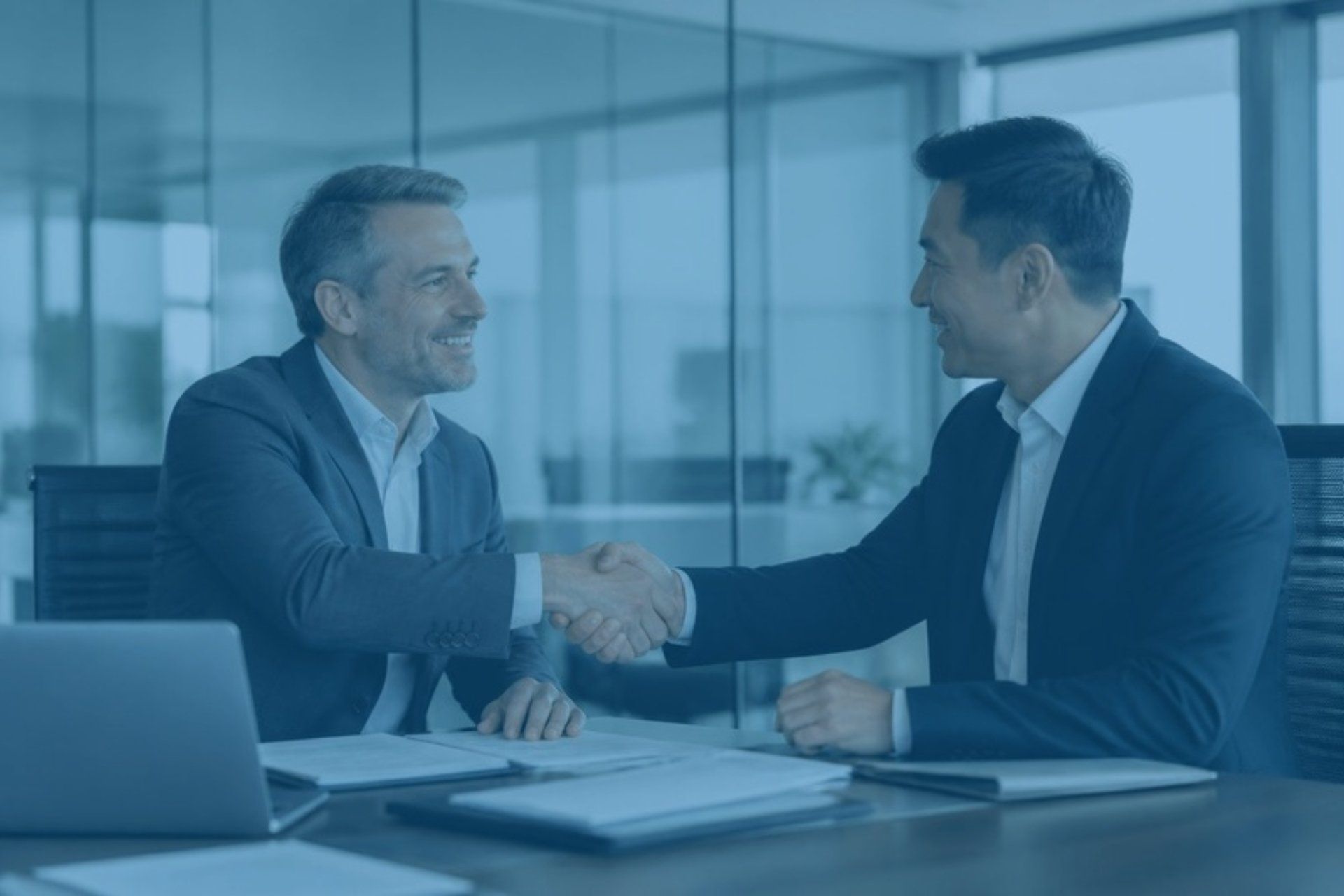 Two executives shaking hands across a conference table after an acquisition meeting