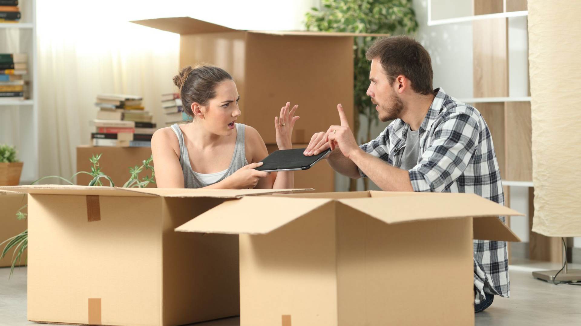 Two people talking amid moving boxes in a bright apartment, unpacking after a move.