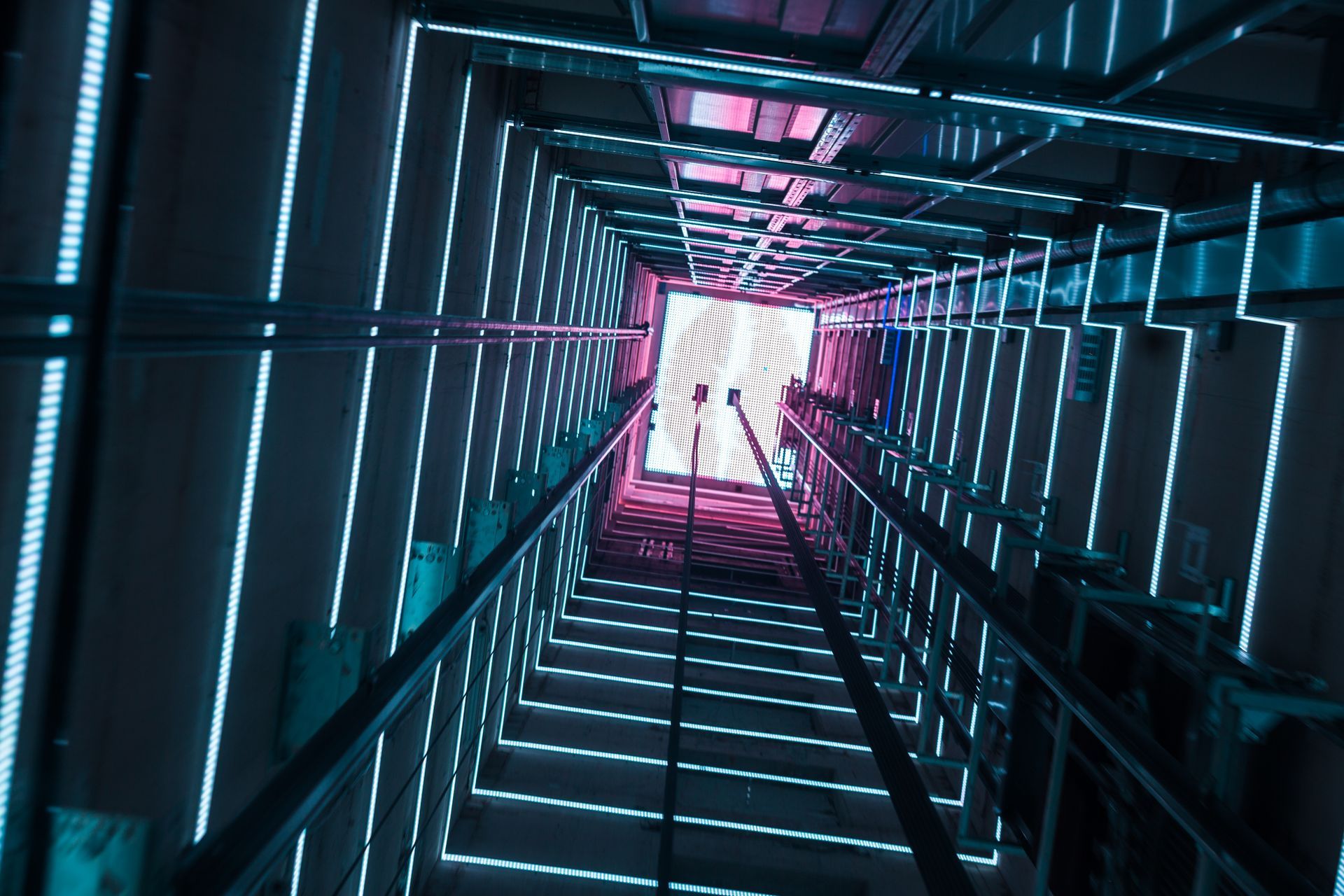 Looking up an illuminated elevator shaft with glowing blue and pink LED lights.