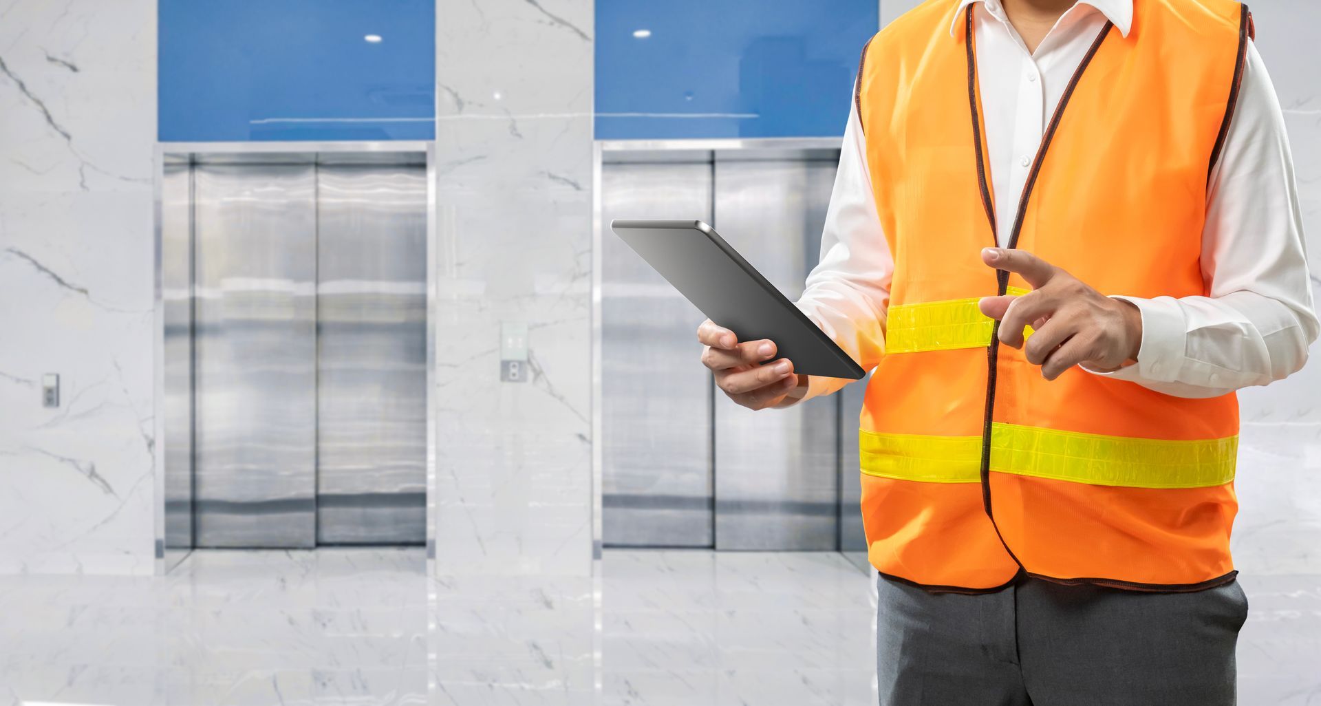 Technician holding a tablet during routine elevator maintenance in a modern office lobby.