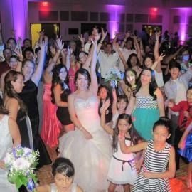 Crowd dancing and posing at a lively indoor party with purple lighting, bride in a white dress centered