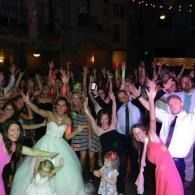 Crowd dancing and cheering at a nighttime wedding reception, with arms raised on the dance floor.