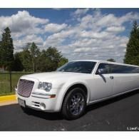 White luxury limo parked outdoors under a cloudy sky on a road with trees and a yellow curb.