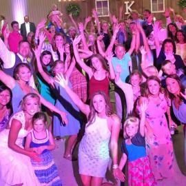 Crowd dancing with raised hands under pink lighting at an indoor party