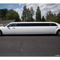 White stretch limousine parked on a road with trees and cloudy sky in the background