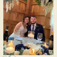 Wedding couple seated at a candlelit reception table with white flowers and blue accents
