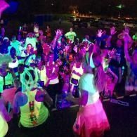 People dancing in neon-lit costumes at a nighttime party or event