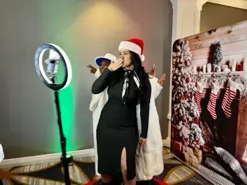 Woman in Santa hat posing beside a ring light and holiday photo backdrop