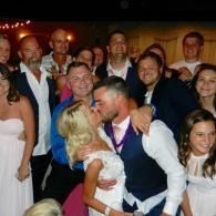 Couple kissing at a formal indoor party, surrounded by smiling guests