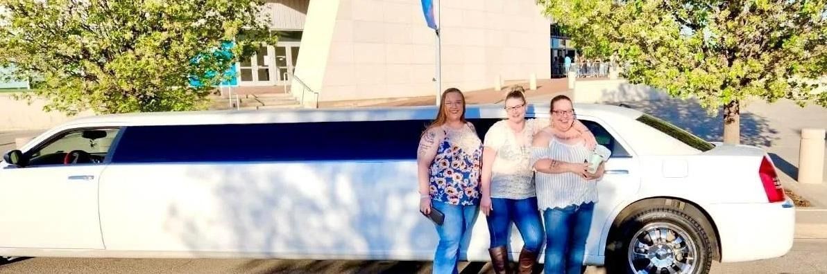 Three people standing beside a long white limousine in front of a building.