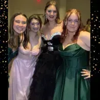 Four people in formal dresses posing together at a party, smiling at the camera.