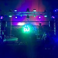 Nighttime outdoor stage with bright purple and blue lights and a glowing green sign in the center