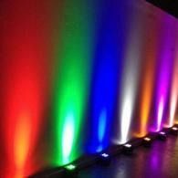 Colorful wall uplights casting red, green, blue, purple, and warm glows along a hallway wall.
