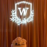 Illuminated white monogram in a shield above orange drapes with flowers below