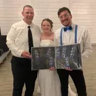 Three people at a wedding, holding an open photo album and smiling indoors.