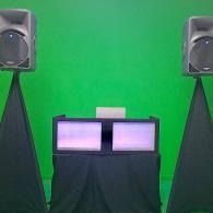 Two glowing screens on a black stand against a bright green backdrop, flanked by two speakers.