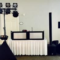 DJ booth and lighting setup at an event venue, with white draped table and tall black speaker stand