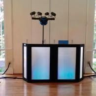 Black speaker box with blue-lit panels beneath a mounted sensor array in a room