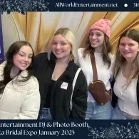 Four smiling women posing at a bridal expo photo booth with a gold backdrop and event banner