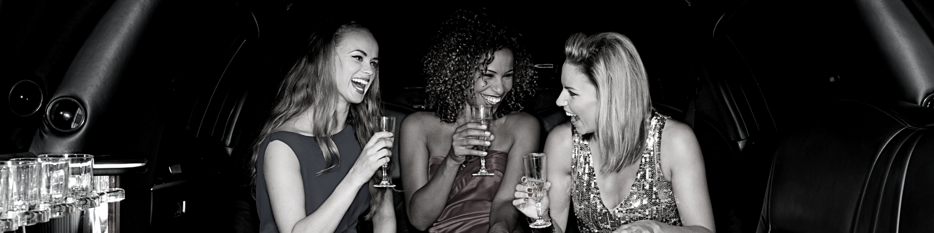 Three women at a nightclub table, laughing and talking with drinks under dim lights