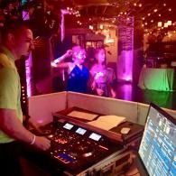 DJ mixing music at a nightclub, with dancers under pink and purple lights