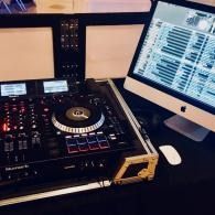DJ controller setup beside a desktop monitor with music software open, on a dark desk