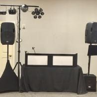 Empty DJ booth with speakers and stage lighting on a plain indoor stage