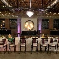 Elegant event hall with rows of chairs facing a lit stage and chandelier under string lights