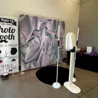Photo booth setup with backdrop, sign, and two white stands in a room