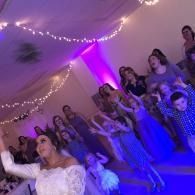 Group dancing at a party under purple and blue lights, with string lights in the background