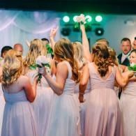 Guests in pale dresses dance at a wedding reception under green stage lights