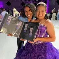 Two young ladies in purple dresses holding a photo collage binder/folder at a decorated indoor celebration