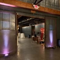 Industrial venue entrance with concrete pillars lit purple, opening into a room with tables and chairs inside