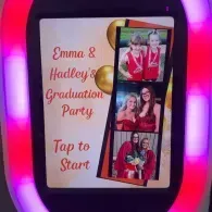 Emma & Hadley graduation party sign with pink lights and three photos, reading “Tap to Start.”