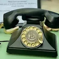 Vintage black rotary telephone with gold dial and handset on a green surface