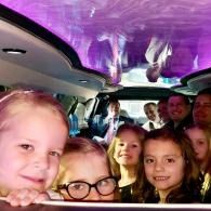 Group of people smiling inside a purple-lit limo cabin, looking toward the camera