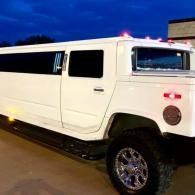 White stretch Hummer limousine parked at night with red lights on and chrome wheels