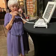 Woman in a purple dress speaking into a phone beside a white device on a black table outdoors