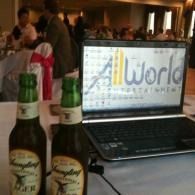 Two beer bottles in front of a laptop displaying the iWorld logo in a dimly lit room