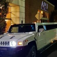 White stretch Hummer limousine parked at night outside a lit building entrance