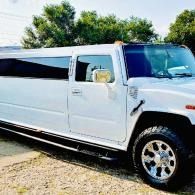White stretch limousine parked outdoors on gravel, with tinted windows and chrome wheels.