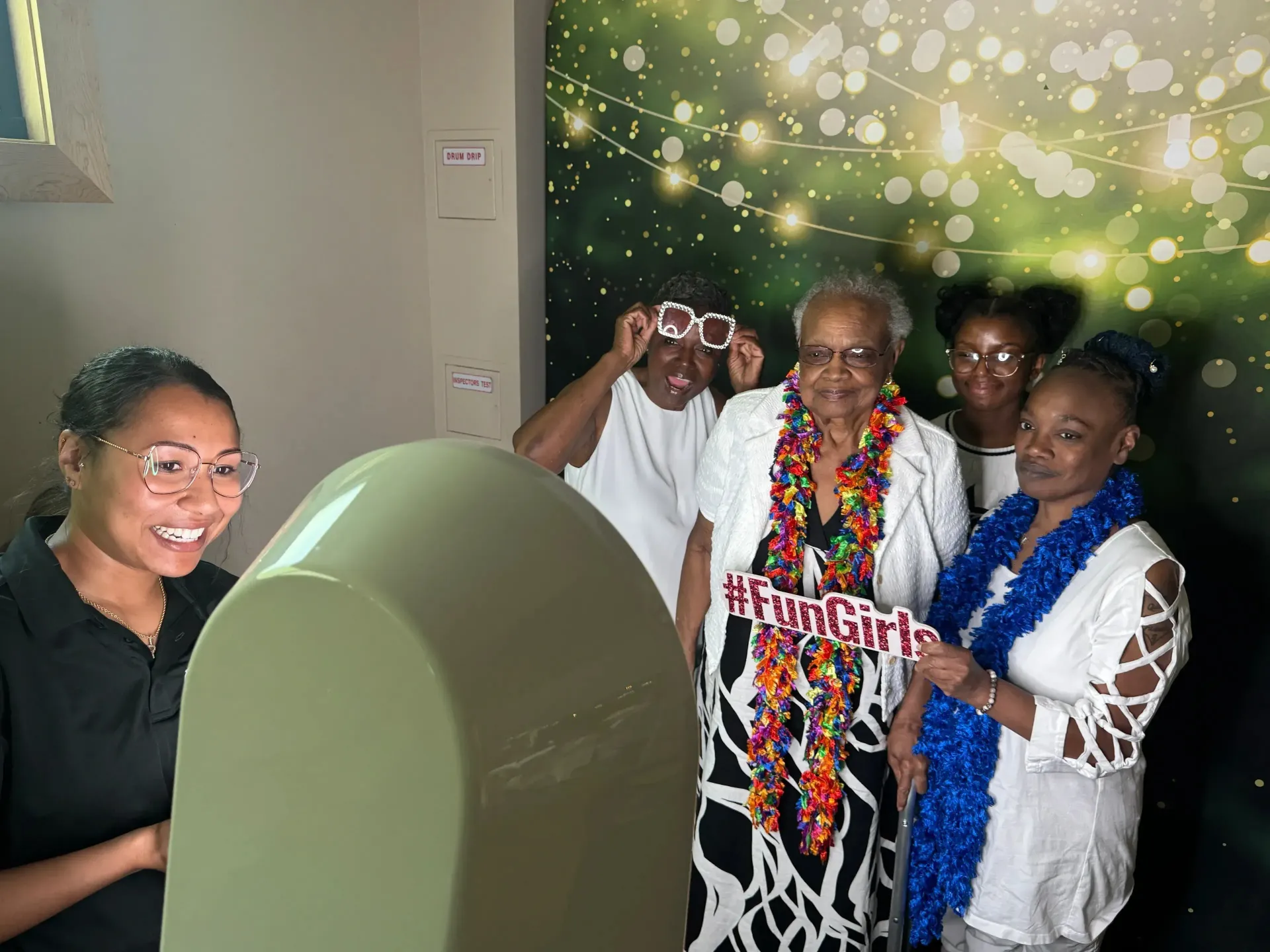 Five people posing beside a green display, smiling in a decorated indoor setting