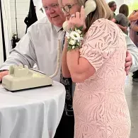 Woman in a pink dress speaking on a beige rotary phone at a table during an event