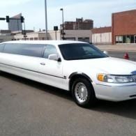 White stretch limousine parked on a street in front of industrial buildings.