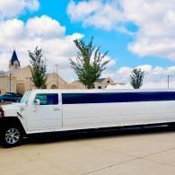 White stretch limousine parked on a street under a cloudy sky, with buildings and trees in the background