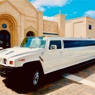 White stretch limousine parked beside a beige stone building under a bright blue sky
