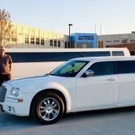 White stretch limousine parked outside a building at sunset, with a person standing beside it.
